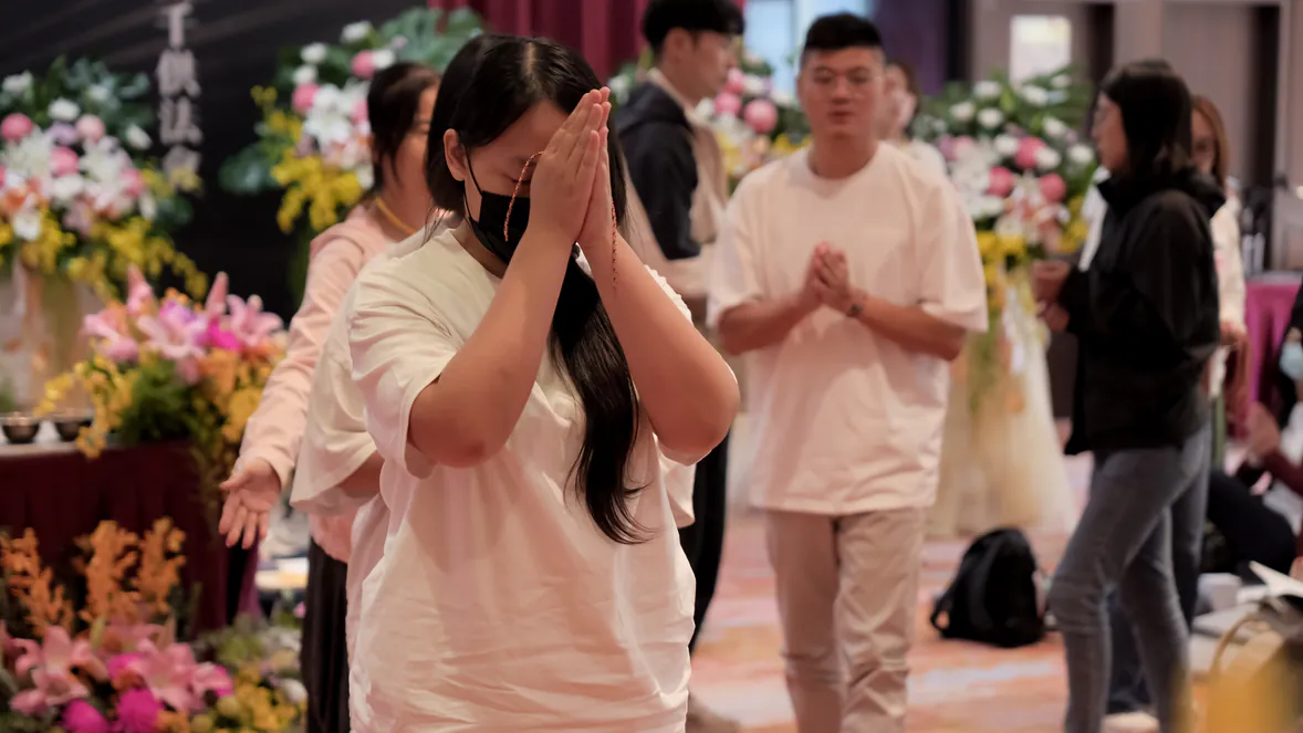 與會者在滿場供花的法會現場閉目合掌祈願